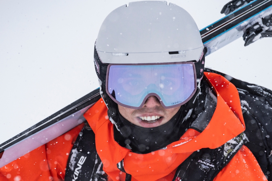 A man dressed for skiing with an orange jacket, white helmet made from ARPRO and backpack